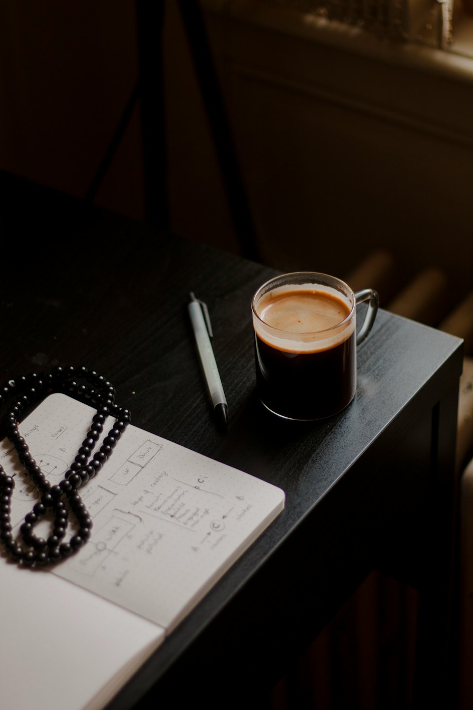 A black desk with an open notebook, coffee, and pen.