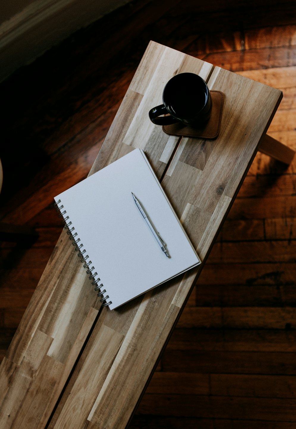 A notebook, pencil, and coffee mug sit on a wooden table.